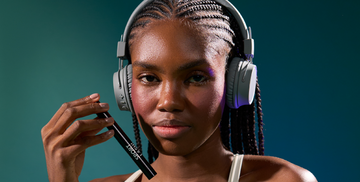 Close-up of a young African-American woman wearing headphones, holding Motion Beauty Sport Lash Waterproof Mascara.