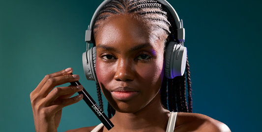 Close-up of a young African-American woman wearing headphones, holding Motion Beauty Sport Lash Waterproof Mascara.