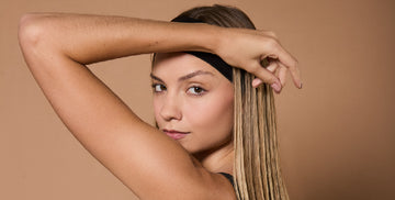 Close-up of a young blonde woman holding her left arm up over her head, looking at the camera.