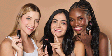 Three diverse young women in sports outfits, smiling and showcasing Motion Beauty Blush Up! Lip and Cheek Sticks.