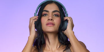 Close-up of a young black-haired woman putting her headphones on, on a light purple background.