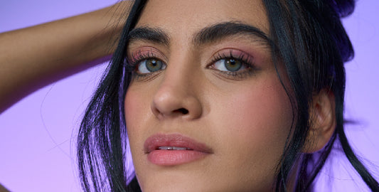 Close-up of a young woman with soft makeup on, holding her black hair up, looking at the camera.