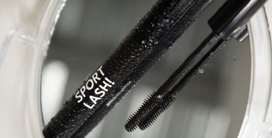 Close-up of a wet Motion Beauty Sport Lash Waterproof Mascara with its brush by its side, over a mirror.