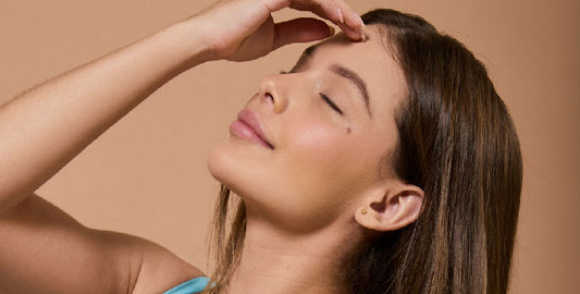 Close-up of a young woman with closed eyes, looking up, touching her forehead with a serene expression