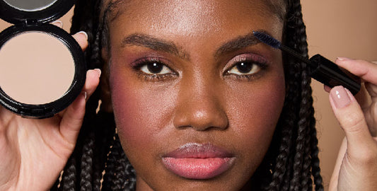 Close-up of a young African-American woman getting her makeup done, with Set & Last Setting Powder on the left and Fix & Go brush on her eyebrows.