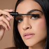 Close-up of a young woman's face with dark hair, using a mascara brush to apply Motion Beauty Sport Lash Waterproof Mascara.